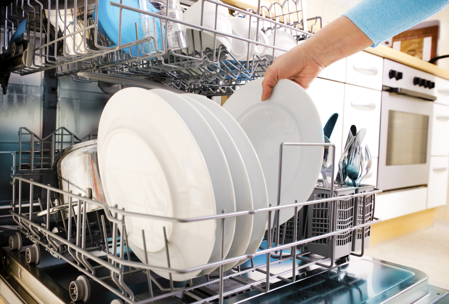 A person loads clean plates into a dishwasher