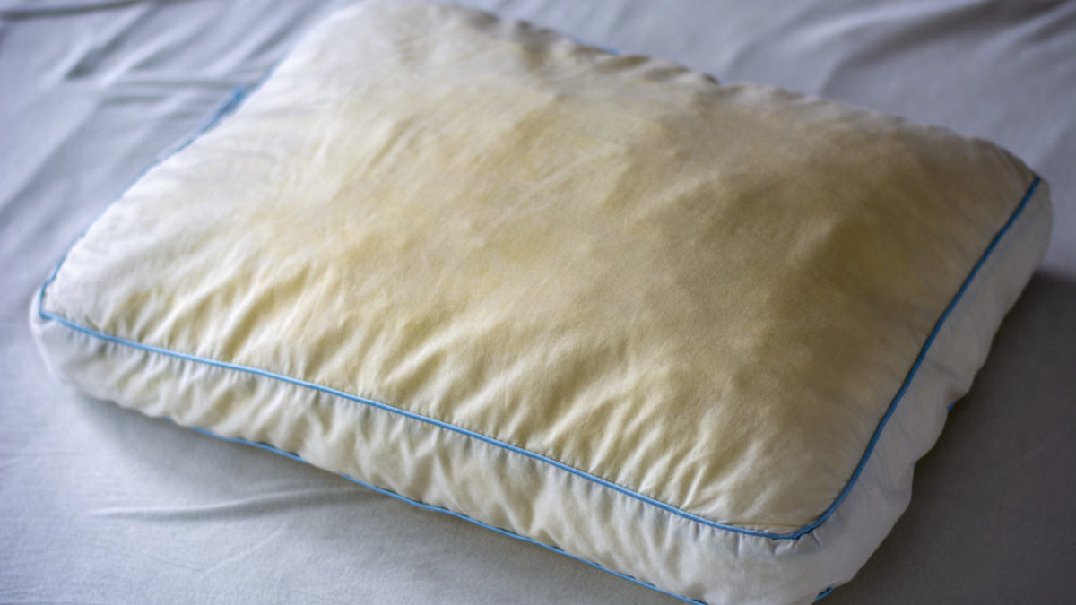 Old dirty used yellow sweat stained pillow on a mattress