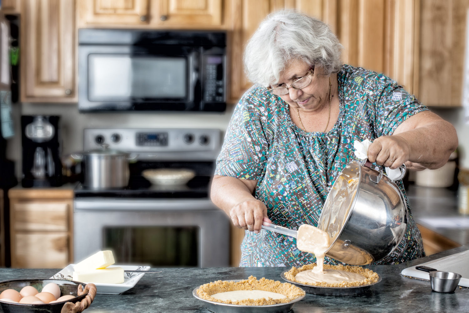 Photo of a grandmother elderly active woman in a natural kitchen filling pies. White older woman in the kitchen baking.