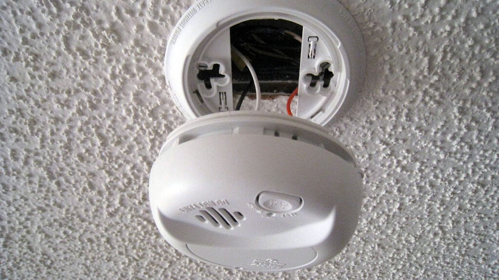 a hardwired smoke detector hangs from a ceiling
