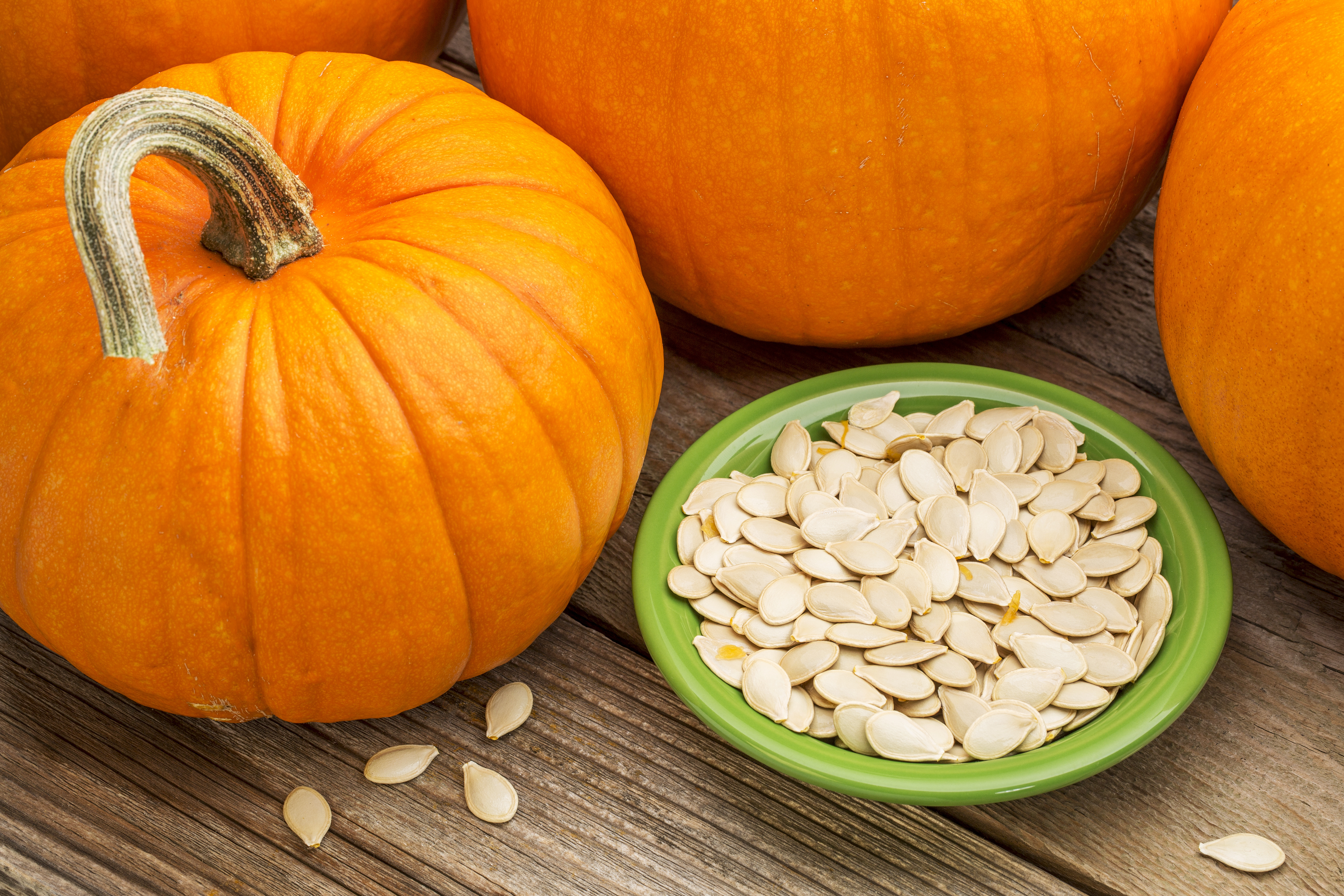 Bowl of pumpkin seeds with pumpkins