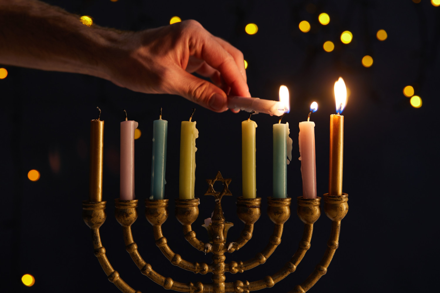 cropped view of man lighting up candles in menorah on black back