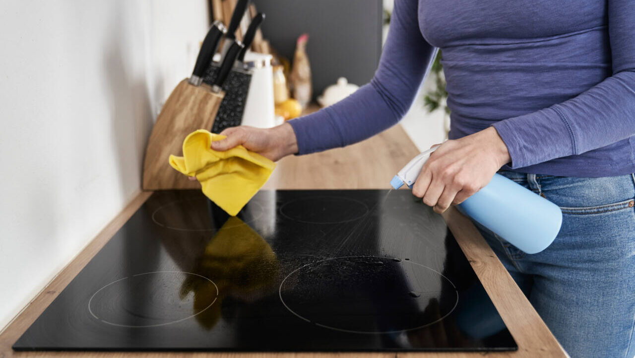 woman cleaning glass cooktop with spray bottle and cloth