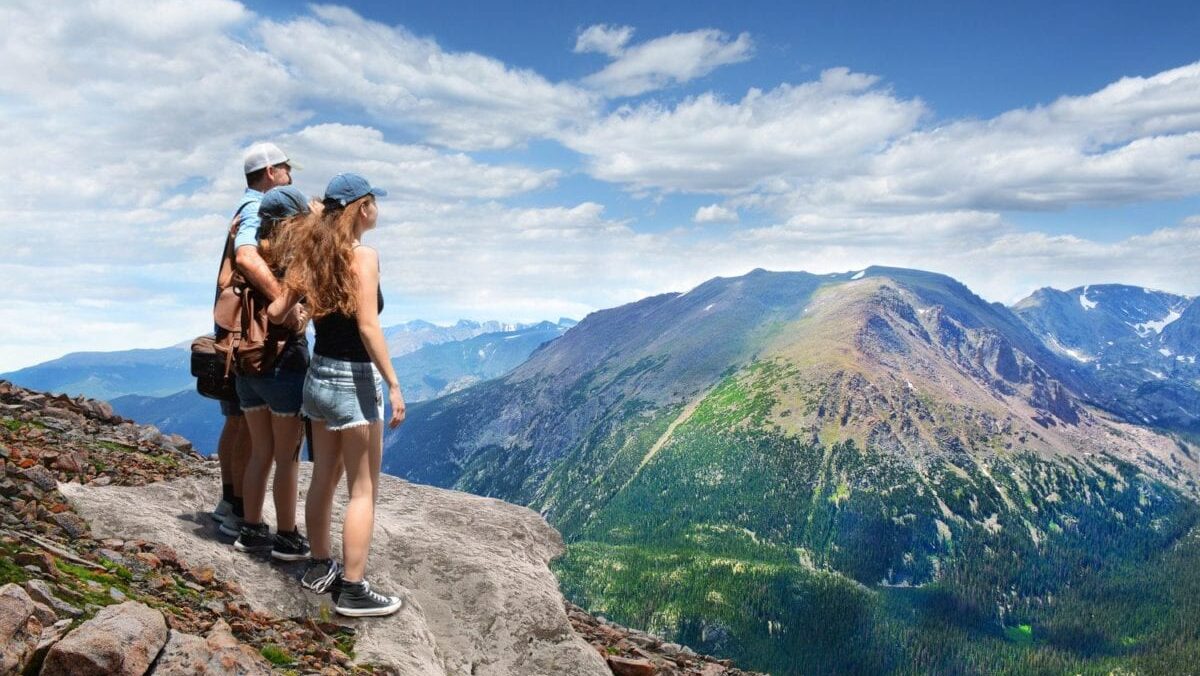 Family of three looking at beautiful summer mountains landscape, on hiking trip, on top of mountain rock
