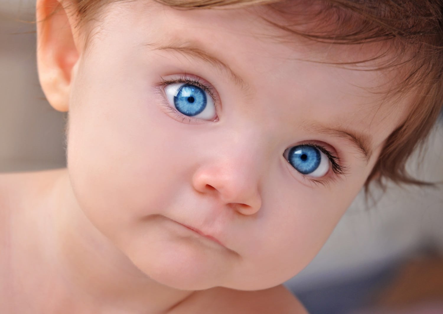 A young little baby is looking at the camera with bright blue eyes. Use it for a child or parenthood concept.