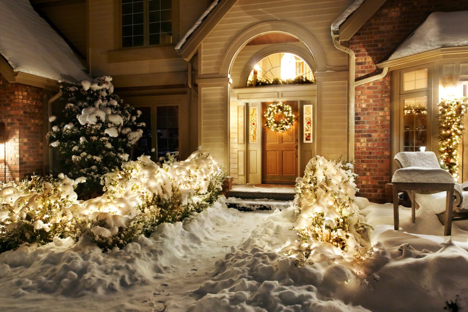 Outside Christmas lights line path to a front door on a snowy evening