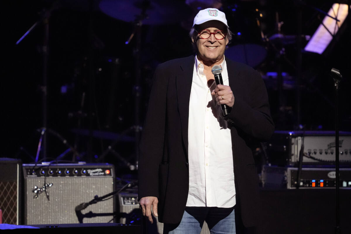 Chevy Chase stands onstage with microphone