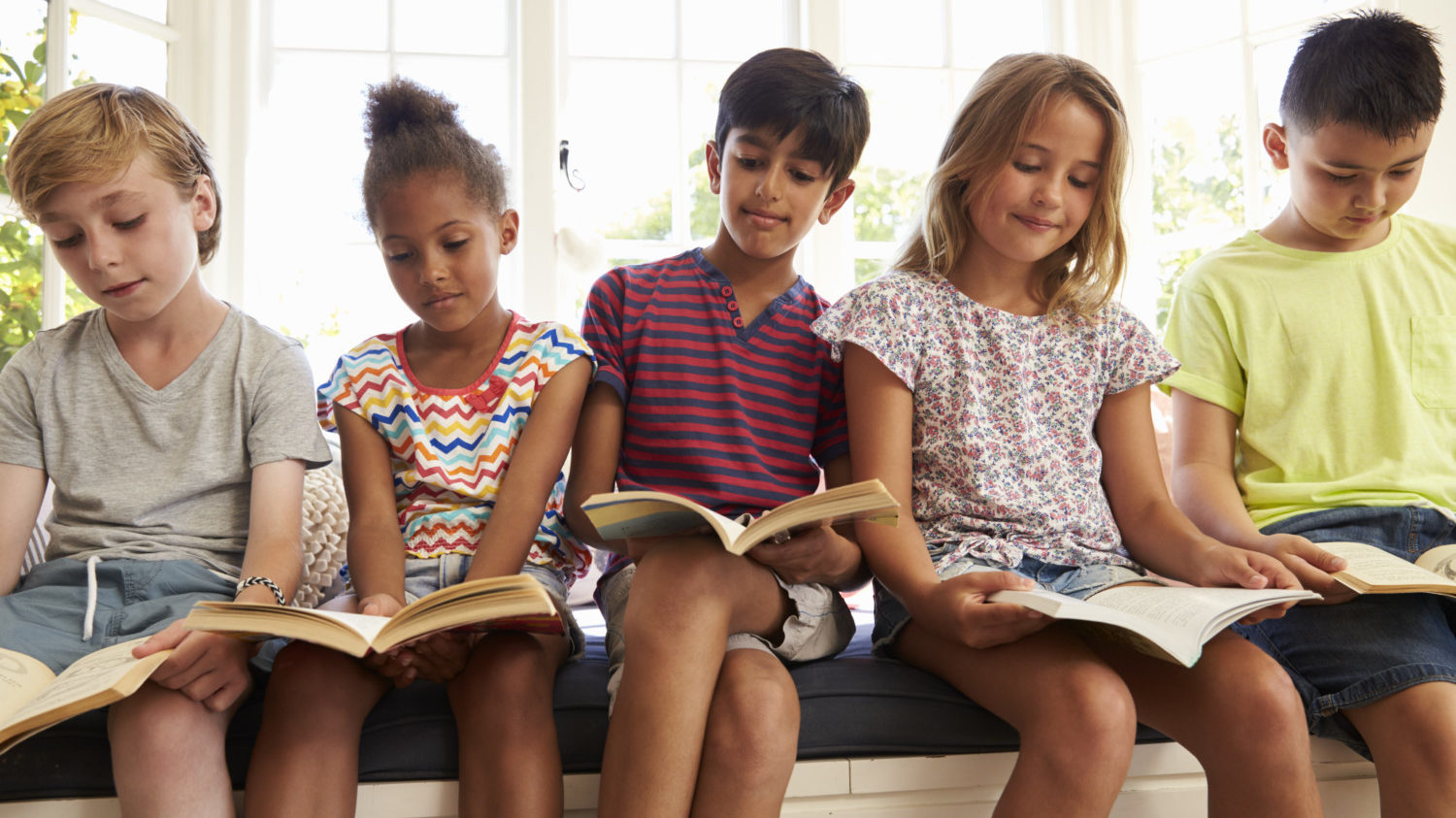 Group Of Children Reading books On Window Seat