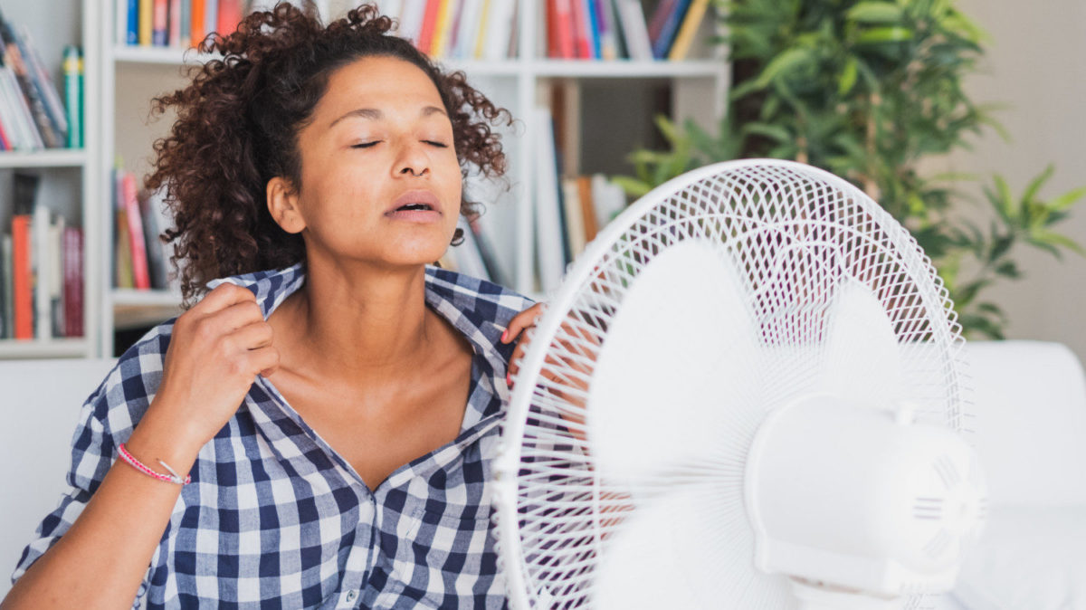 A woman feeling hot and sitting in front of a fan.