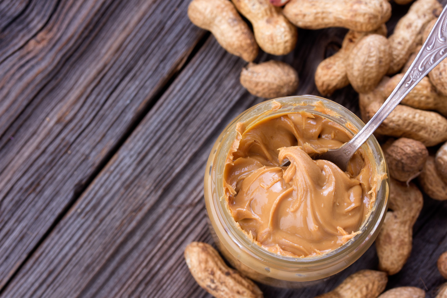 Fresh made creamy Peanut Butter in a glass jar and peanuts on old wooden table.