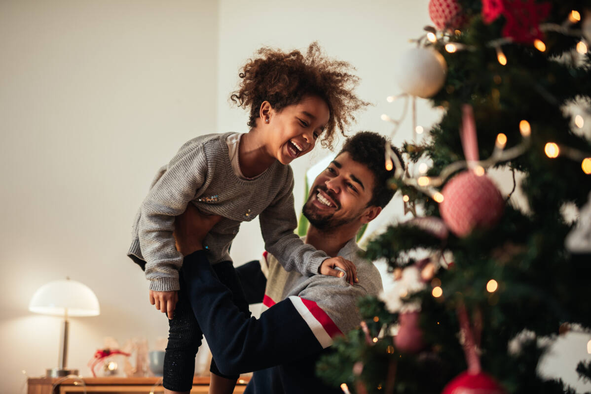 Dad hoists daughter into the air next to Christmas tree