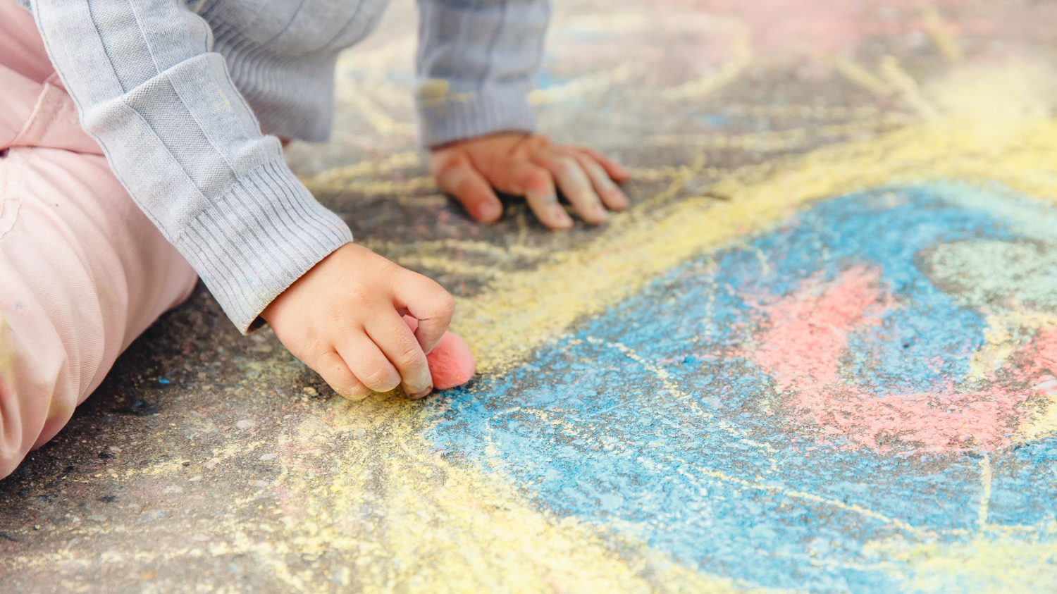 Child draws hand in colored chalk drawing on pavement. Top view