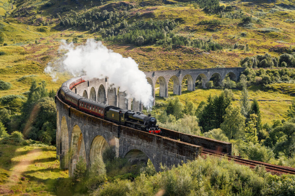Steam train chugs along Glenfinnan Viaduct in Scotland 