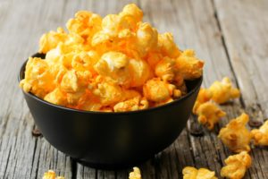 cheese popcorn in a black bowl on wooden background