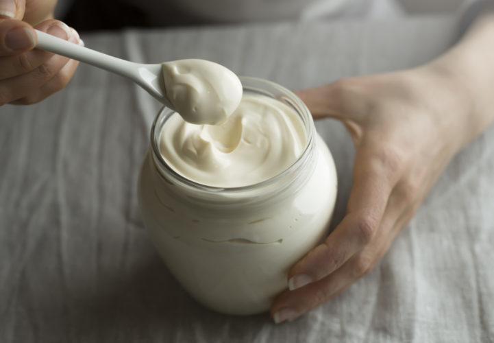a pot of sour cream with a spoon held by someone