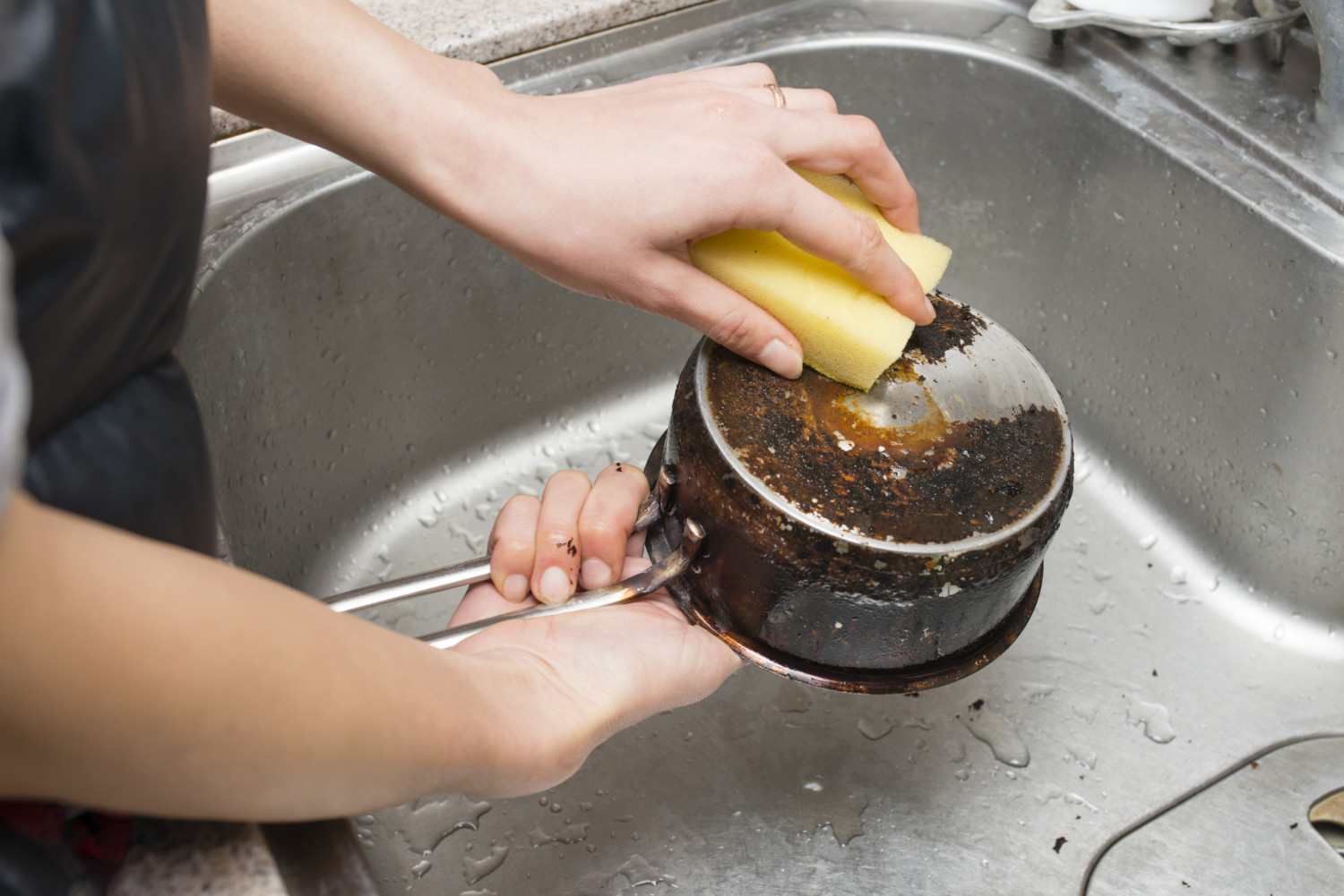Hands scrub baked-on grease on cookware