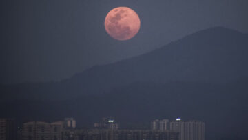 Pink full moon rises over a mountain town