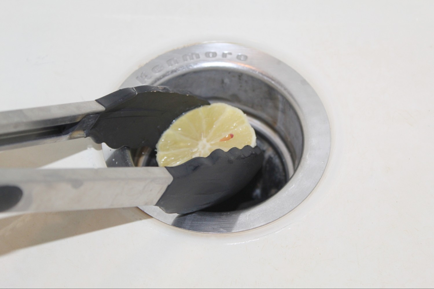 tongs placing lemon half in garbage disposal