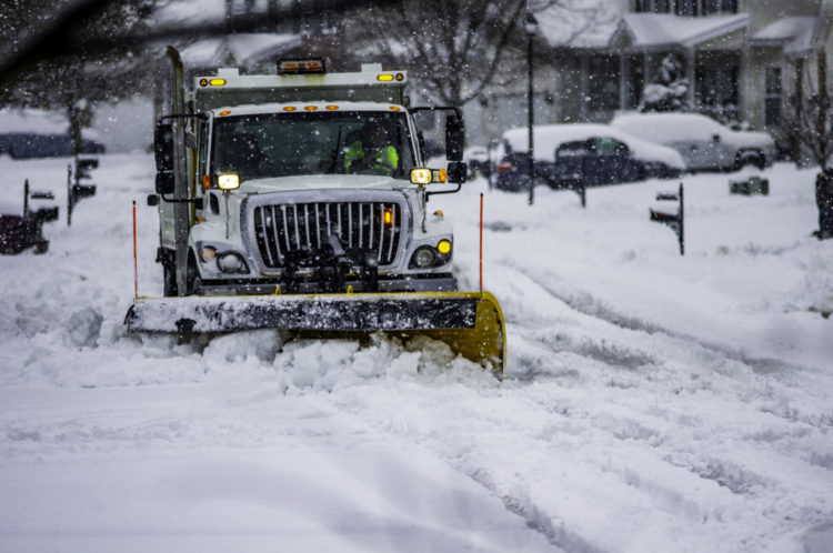 White snowplow truck plows snow on neighborhood street
