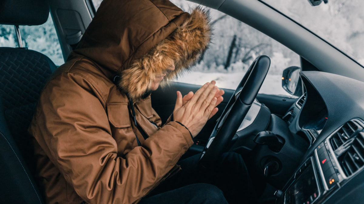 Man in down jacket tries to keep warm and not freeze in his stalled car in winter. The concept of a dangerous accident or heater failure in the cold season