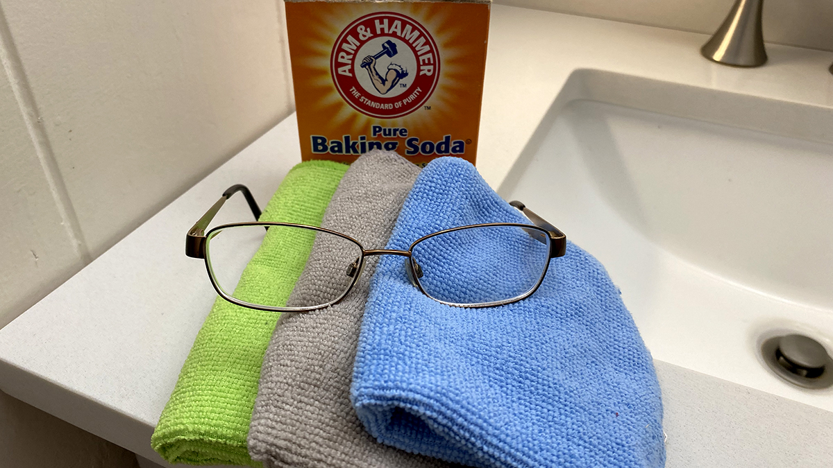 Bright green, gray and light blue microfiber cloths with a pair of glasses on top of them and a box of Arm & Hammer baking soda behind it
