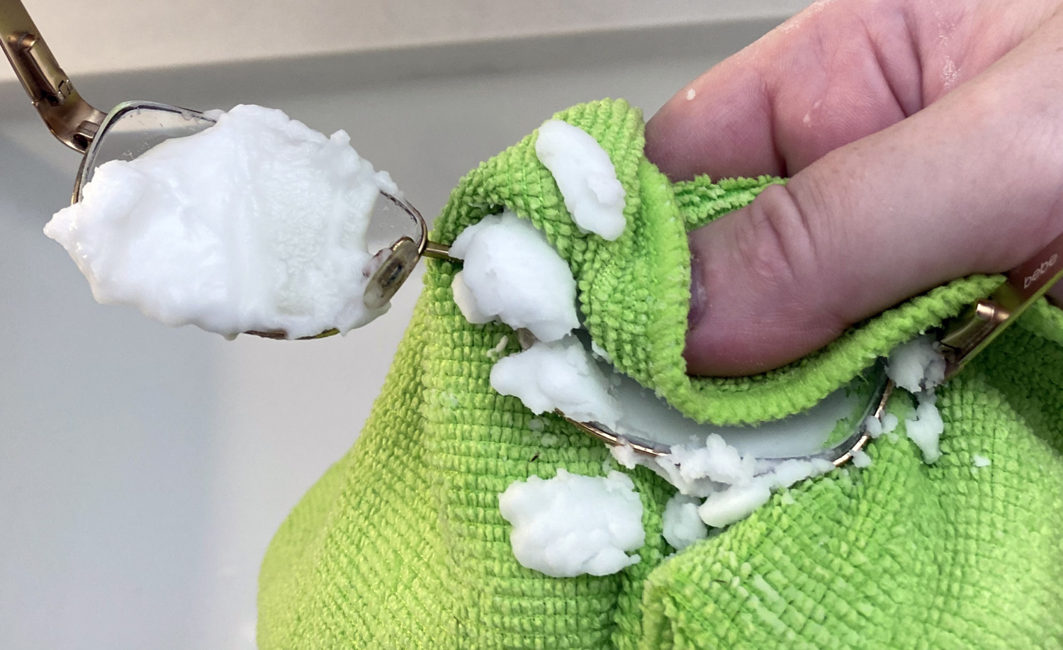 hand using green microfiber cloth to rub white baking soda paste on glass lenses