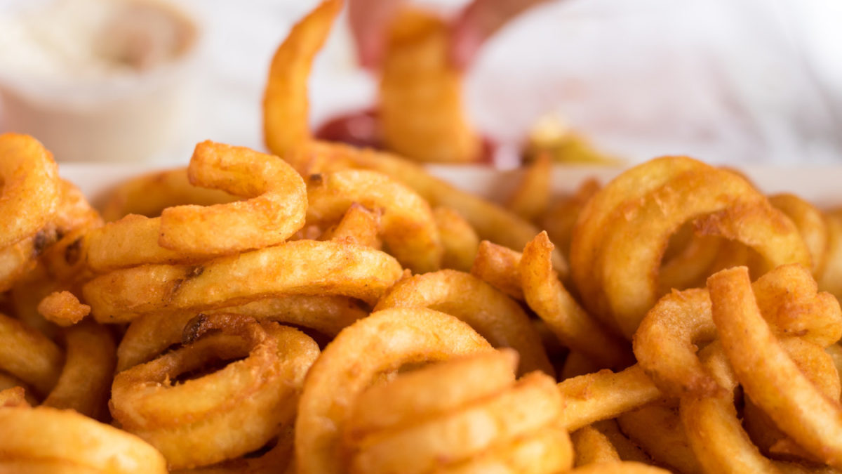 Curly fries with hand dipping one in ketchup