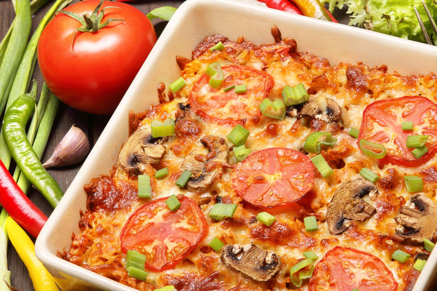 Casserole with tomato and mushrooms on a wooden background