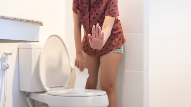 Woman showing hands stop with sanitary napkin flushed down toilet.