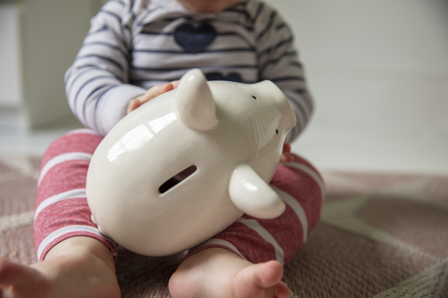 Young baby holds onto a white piggy bank.