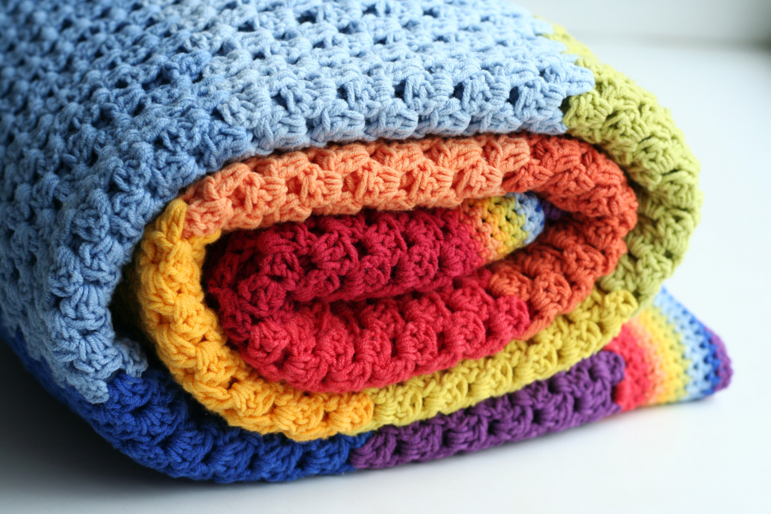 A rainbow crocheted blanket rolled up.