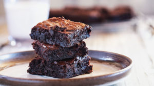 A stack of three gooey, fudgy brownies on a plate near a glass of milk.