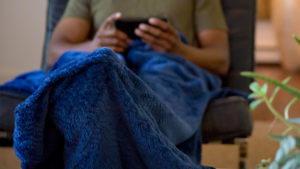 Man uses a PediPocket blanket on the couch. The blanket has a pocket to keep feet covered.