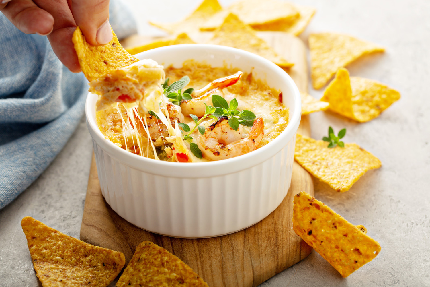 a hand scoops up a chip with hot seafood dip on it from a ramekin filled with cheesy seafood-crab dip surrounded by tortilla chips
