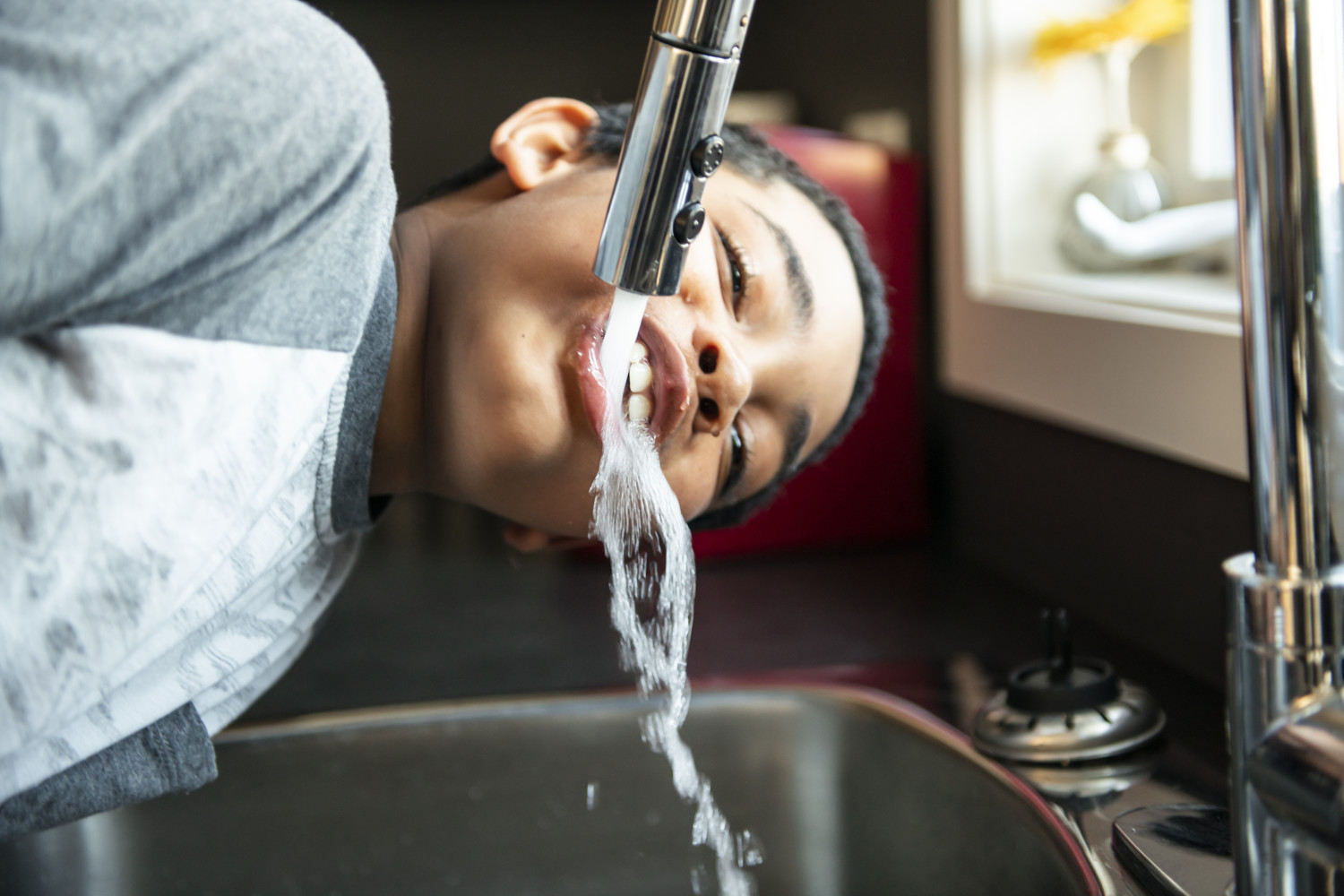 Boy drinks tap water from kitchen faucet