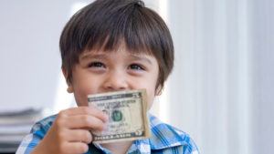 Little boy smiles with a $5 bill.