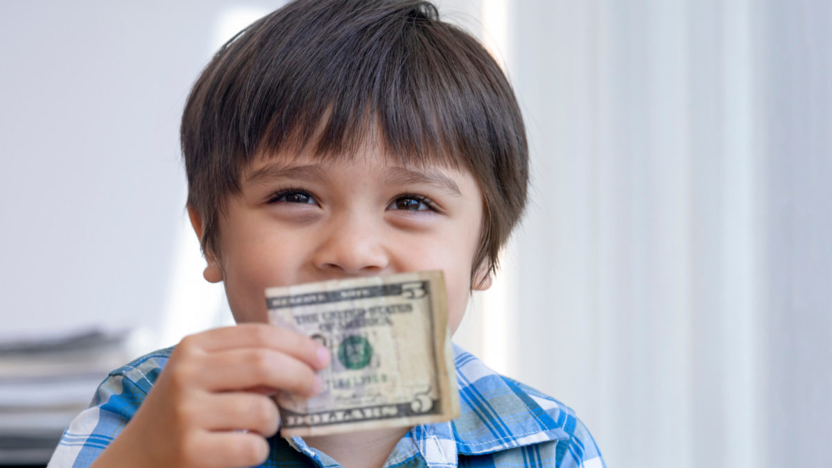 A little boy smiles with a $5 bill.