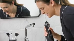 A woman uses a cordless Waterpik water flosser in her bathroom.