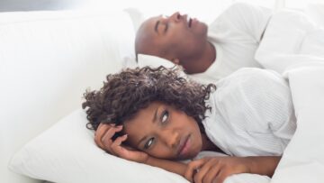 Annoyed woman lying in bed with snoring boyfriend