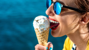 Young woman in yellow sweater and sunglasses eating ice cream in a cone.
