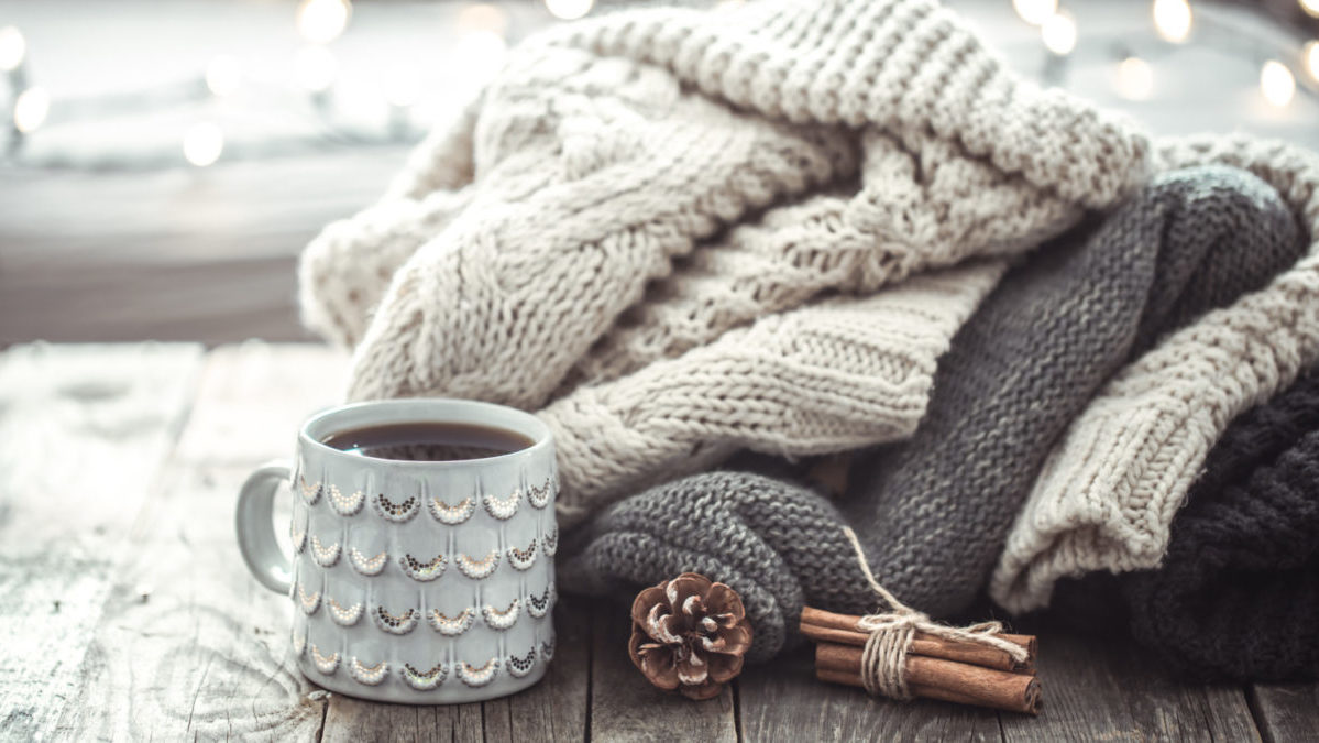 Fall sweaters lay in a pile next to a cup of hot coffee.