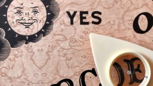 A Ouija board and planchette are shown in close-up.