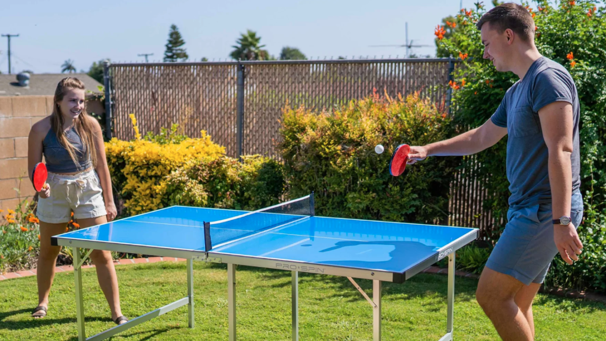 Two people play outdoors on a Pro-Spin midsize ping pong table.