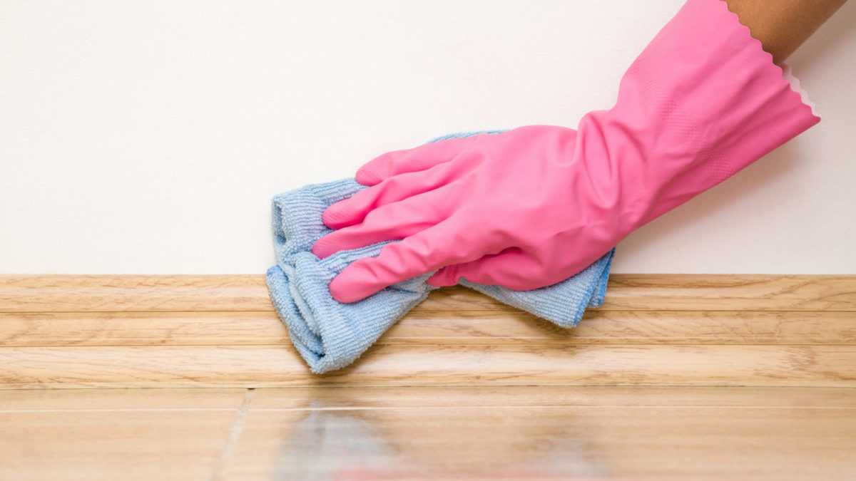 Hand in rubber protective glove cleaning baseboard on the floor