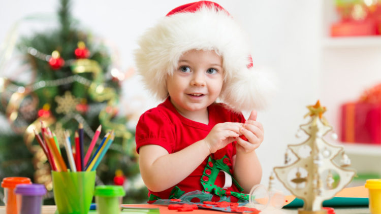 A little girl makes Christmas crafts while wearing a Santa hat.
