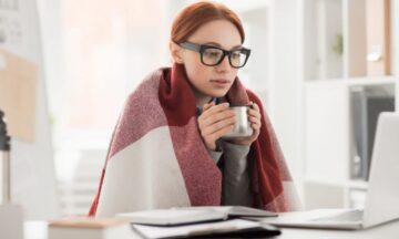 cold woman at computer desk holding mug