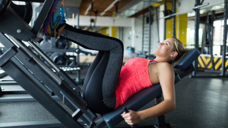 A woman does leg presses at a gym.