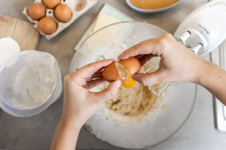 Baker cracks egg over bowl while baking