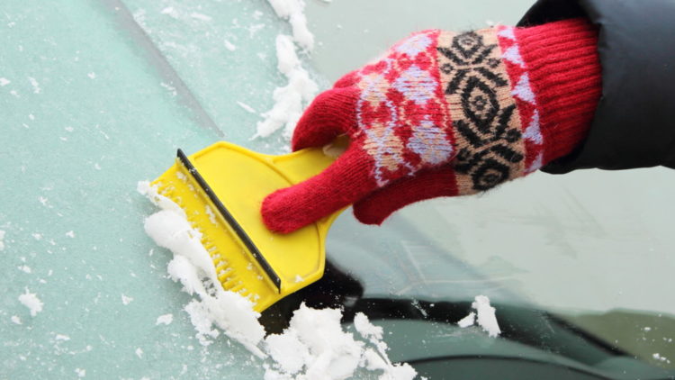 Gloved hand uses ice scraper on frozen windshield
