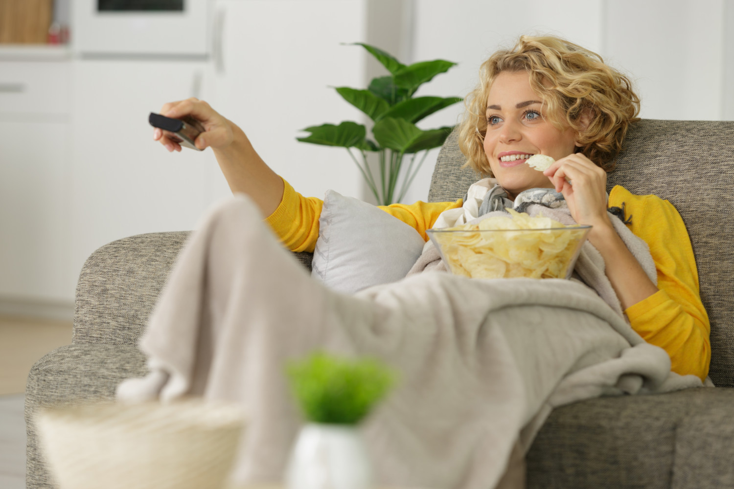 Woman watches TV with blanket and bowl of chips